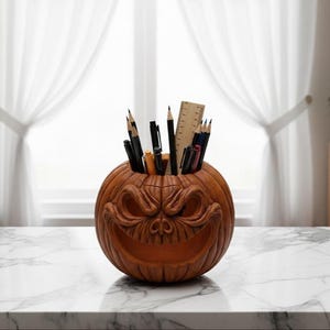 May include: A brown, carved pumpkin-shaped desk tidy with a grinning face. The pumpkin is filled with pencils, pens, and a wooden ruler. The organiser sits on a white marble surface in front of a window with white curtains.