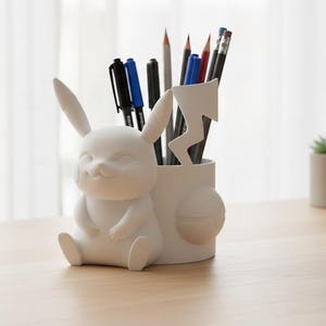 May include: A white Pikachu-shaped desk organizer holding pens and pencils. The organizer features a smiling Pikachu figure with long ears and a cylindrical holder with a lightning bolt design. The desk accessory is made of a smooth, matte material.