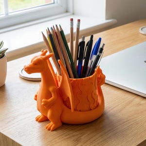 Könnte beinhalten: Ein orangefarbener, drachenförmiger Schreibtisch-Organizer mit Bleistiften und Stiften. Der Organizer besteht aus Kunststoff und hat ein detailliertes Design eines Drachen mit Flügeln und Flammen. Er steht auf einem Holzschreibtisch.