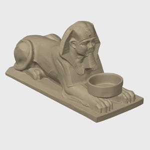K&ouml;nnte beinhalten: Beigefarbene Sphinx-Statue mit einer Schale. Die Sphinx liegt in einer liegenden Position, Kopf und Brust sind erhoben. Die Schale ruht auf den Pfoten der Sphinx. Die Statue steht auf einem rechteckigen Sockel.