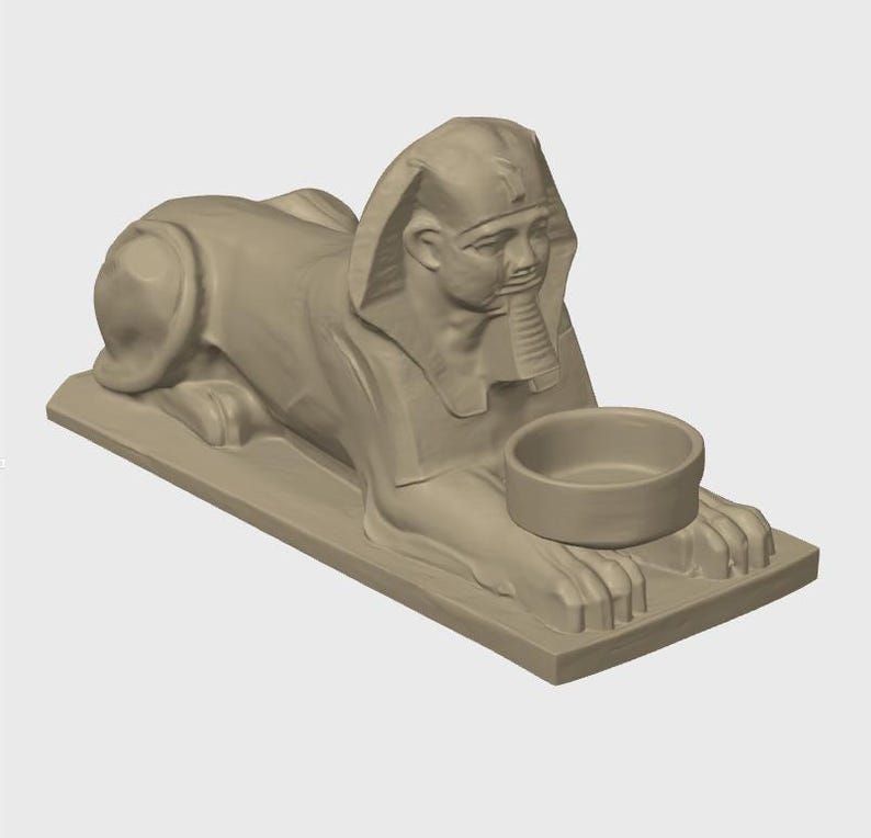 K&ouml;nnte beinhalten: Beigefarbene Sphinx-Statue mit einer Schale. Die Sphinx liegt in einer liegenden Position, Kopf und Brust sind erhoben. Die Schale ruht auf den Pfoten der Sphinx. Die Statue steht auf einem rechteckigen Sockel.