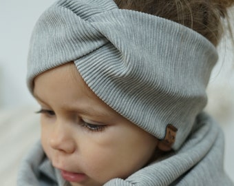 May include: A gray ribbed knit headband with a knotted design. The headband is worn by a young child with a gray scarf.