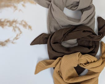 May include: Three cotton muslin squares in beige, brown, and mustard yellow. The squares are folded and stacked on top of each other.