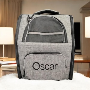May include: Gray pet carrier backpack with a mesh window and a zippered pocket on the front. The pocket has the name "Oscar" embroidered on it.