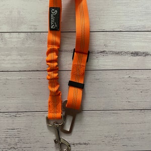 May include: Orange retractable dog lead with a metal clip and a black seatbelt attachment. The lead has the word "SLAMZ" printed on it.