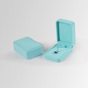 May include: A light blue velvet jewelry box with a hinged lid, open to reveal a silver necklace with a blue gemstone pendant.