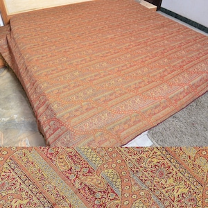 Puede incluir: Una manta de tiro de color rojo, dorado y crema con un diseño de paisley. La manta está hecha de un tejido suave y tejido y tiene un borde con flecos.