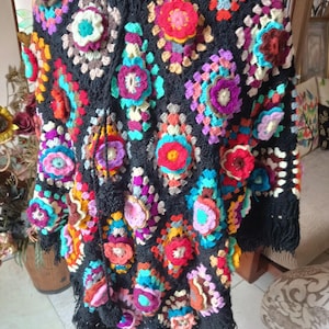 Puede incluir: Un poncho de crochet negro con motivos florales coloridos y ribete de flecos.