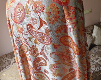 May include: A rectangular shawl featuring a light silver-grey base with an intricate woven paisley pattern in vibrant shades of orange, red, and yellow. The fabric displays a textured finish with repeating floral and teardrop motifs throughout.