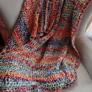May include: A colorful striped crocheted throw blanket in shades of red, orange, yellow, blue, and white. The blanket is draped over a white armchair.