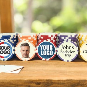 May include: Stacks of personalized poker chips with different designs. One chip features a man's face, another says "Your Logo", another says "Johns Bachelor Trip", and another says "Your Custom Text".