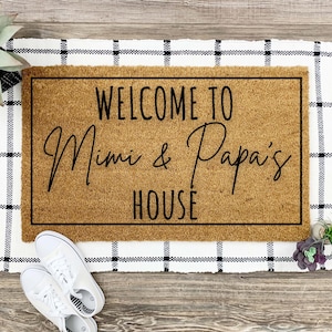 May include: A brown coir doormat with black text that reads "Welcome to Mimi & Papa's House". The doormat is on a black and white checkered rug.