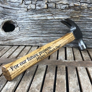 May include: A wooden-handled hammer with a black metal head. The handle is engraved with the text "For our future projects. Happy Father's Day!"