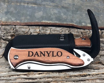 May include: A personalized pocket knife with a wooden handle and a black nylon sheath. The knife has a silver blade and the handle is engraved with the name "DANYLO".