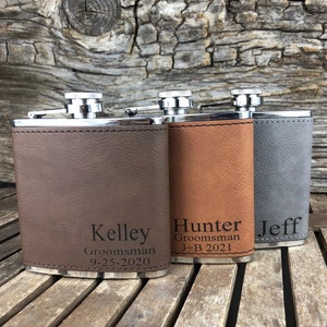 May include: Three personalized stainless steel hip flasks with brown, tan, and gray leatherette covers. The flasks are engraved with the names "Kelley", "Hunter", and "Jeff" along with the text "Groomsman" and dates.