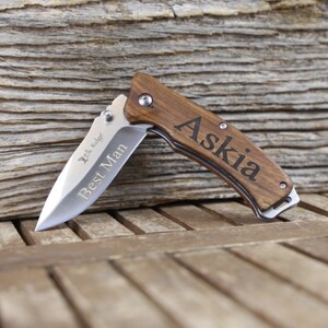 May include: A brown wooden pocket knife with a silver blade. The knife is engraved with the words "Best Man" and "Askia".