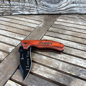 May include: A wooden handled pocket knife with a black blade. The handle is engraved with the words "Poppy" and "I Love You".