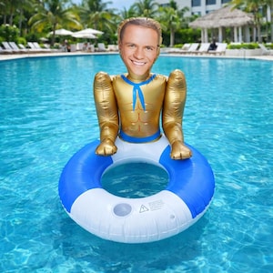 May include: Inflatable pool float shaped like a smiling man with a gold torso, blue accents, and a blue and white inner tube. The float is in a swimming pool with palm trees in the background.