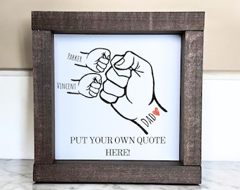 May include: A framed wood sign with a white background and black line art of three fists bumping. The text "Parker", "Vincent", and "I Dad" are written on the sign. The sign says "Put your own quote here!"