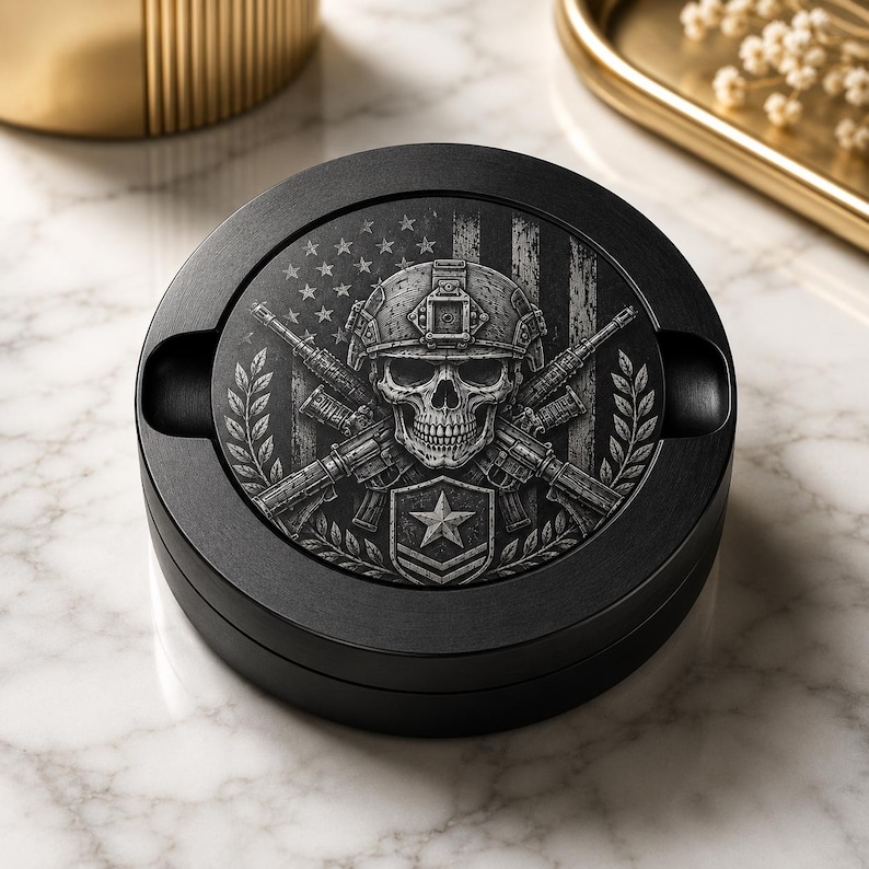 May include: A circular black ashtray with a detailed monochrome graphic on the lid. The design features a skull wearing a tactical helmet, set against a background of two crossed rifles, a star emblem, and a stylised American flag motif.