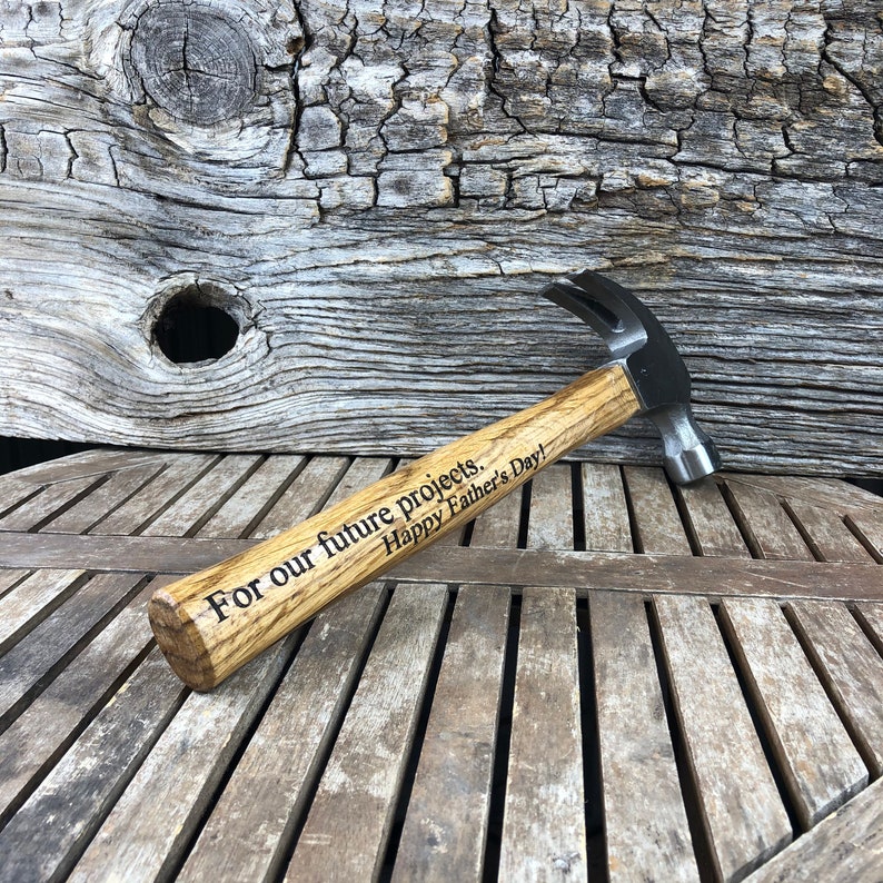 May include: A wooden-handled hammer with a black metal head. The handle is engraved with the text "For our future projects. Happy Father's Day!"