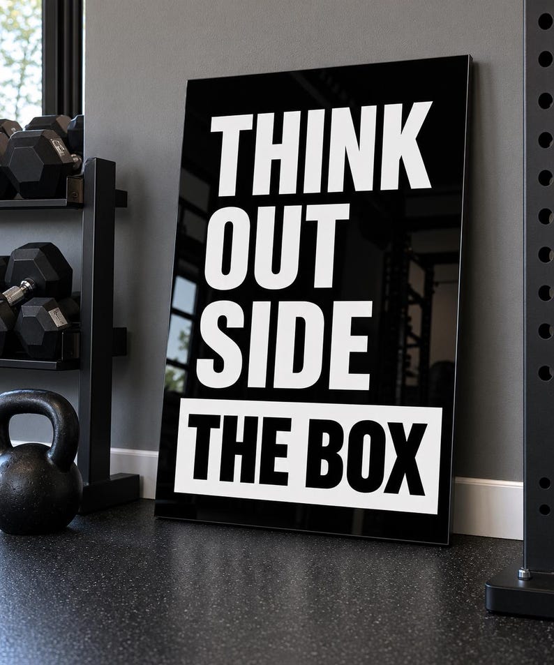 May include: A rectangular black wall sign with white bold sans-serif text that reads THINK OUT SIDE THE BOX. The word THE BOX is printed in black on a white rectangular background at the bottom of the sign, while the other words are white.