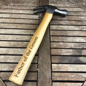 May include: A wooden-handled hammer with a black metal head. The handle is engraved with the words "Father of the Groom".