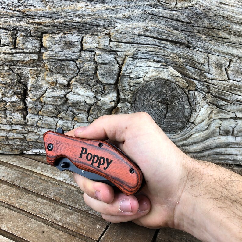 May include: A red and black pocket knife with a wood handle. The knife has the name "Poppy" engraved on the handle.
