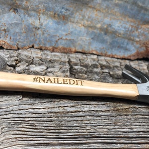 May include: A wooden-handled hammer with a black metal head. The handle is engraved with the text "#NAILEDIT".