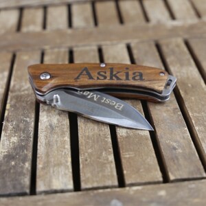 May include: A wooden pocket knife with a stainless steel blade. The handle is engraved with the name "Askia" and the words "Best Man".
