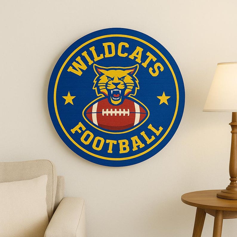 Pu&ograve; includere: Un'insegna da parete circolare blu con una grafica di una testa di gatto selvatico gialla sopra un pallone da football marrone. Il testo WILDCATS &egrave; arcuato in alto e FOOTBALL in basso in lettere maiuscole gialle, con due stelle gialle ai lati.