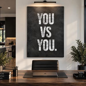 K&ouml;nnte beinhalten: Ein rechteckiges Wandbild mit einem dunklen, texturierten anthrazitfarbenen Hintergrund und dem wei&szlig;en, im Used-Look gedruckten Text "YOU VS YOU." in einer fetten serifenlosen Schrift. Das Kunstwerk ist vertikal an einer Wand angebracht.