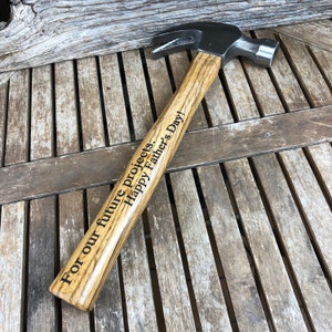 May include: A wooden-handled hammer with a metal head. The handle is engraved with the text "For our future projects. Happy Father's Day!"