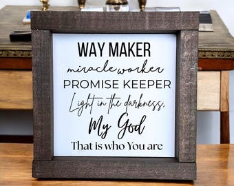 May include: A framed wooden sign with the words "WAY MAKER, miracle worker, PROMISE KEEPER, Light in the darkness, My God, That is who You are" in black script on a white background. The frame is dark brown.