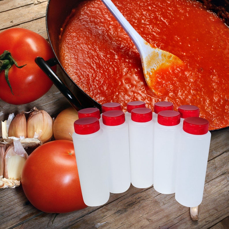 May include: Eight clear plastic bottles with red lids, arranged in a row on a wooden surface. The bottles are filled with a red liquid, possibly tomato sauce. There are tomatoes and garlic cloves in the background.