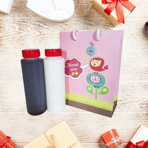 May include: A pink gift bag with a cute bird design and the words "Thank you". Two bottles, one clear and one dark, are in front of the bag.