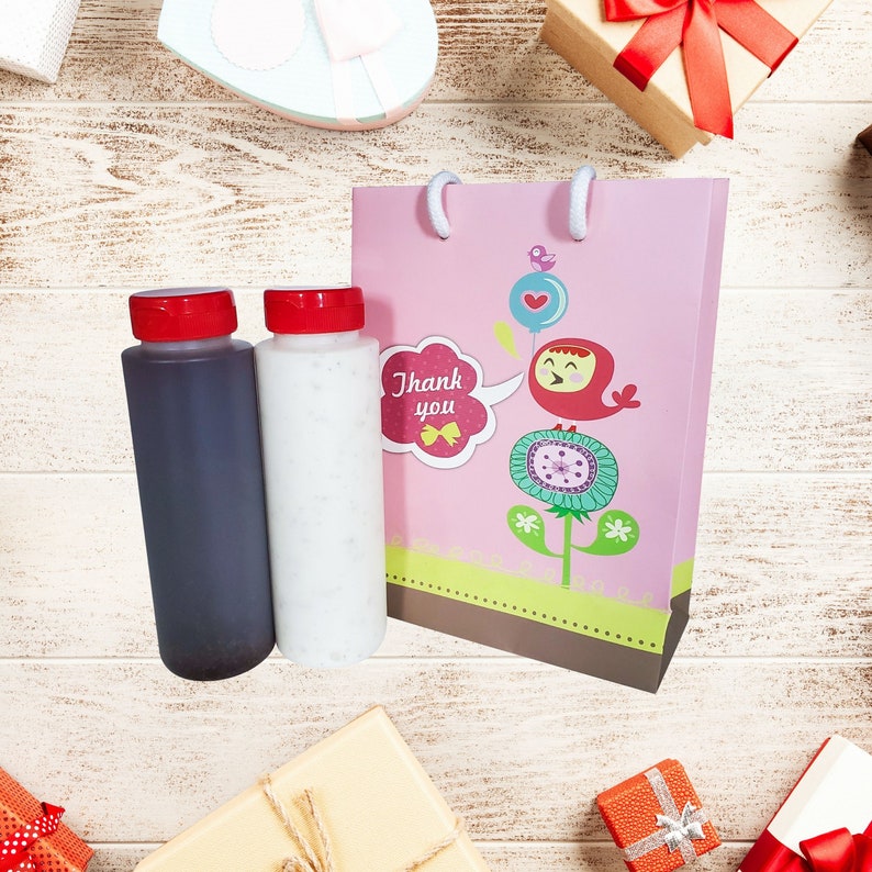 May include: A pink gift bag with a cute bird design and the words "Thank you". Two bottles, one clear and one dark, are in front of the bag.