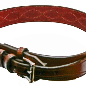 May include: A brown leather belt with a wave-like pattern and a red leather lining. The belt has a silver buckle.
