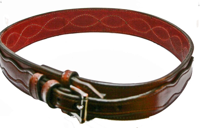 May include: A brown leather belt with a wave-like pattern and a red leather lining. The belt has a silver buckle.