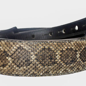 Puede incluir: Un cintur&oacute;n de cuero marr&oacute;n con un patr&oacute;n de piel de serpiente. El cintur&oacute;n est&aacute; doblado por la mitad y el lado de piel de serpiente est&aacute; mirando hacia la c&aacute;mara.