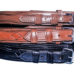 May include: Three leather belts stacked on top of each other. The top two belts are brown with a decorative stitching pattern. The bottom belt is black with a similar stitching pattern.