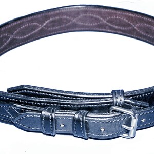 May include: A black leather belt with a silver buckle and a decorative pattern on the inside. The belt is folded in half and the buckle is visible.