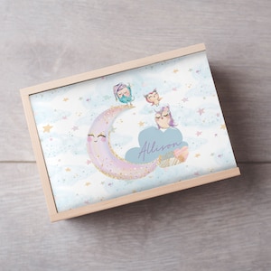 May include: A wooden box featuring a light blue background with a crescent moon adorned with gold glitter. Three owls, wearing sleeping caps, are perched on the moon. The box is personalised with the name "Allison".