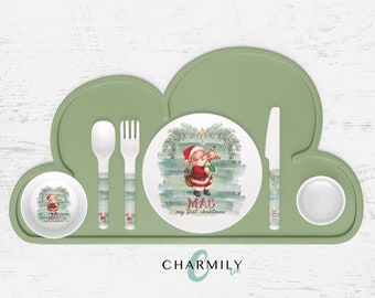 Puede incluir: Un mantel individual de silicona verde en forma de nube con un plato, un tazón y cubiertos blancos. El plato tiene un diseño navideño con un Papá Noel de dibujos animados y el texto "MAG my first christmas".