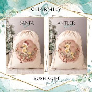 May include: Two personalized Christmas gift bags with drawstring closures. The bags are made of natural canvas fabric and feature a watercolor illustration of a kookaburra bird with a Santa hat and an antler crown. The bags are labeled "Oliver" and "Grace" with the text "Santa hat" and "Antler crown" above the illustrations. The text "Bush Gum australiana" is printed below the bags.