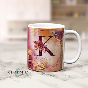 Puede incluir: Taza de cerámica blanca con un diseño floral que presenta una gran letra K y el nombre "Katherine" en una fuente de escritura. El diseño floral está en tonos de rosa, morado y amarillo.