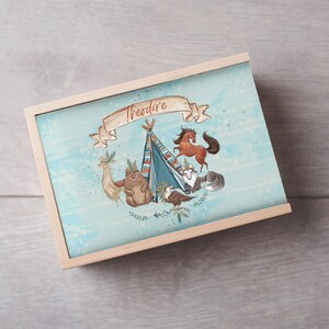 Puede incluir: Una caja de madera con un fondo azul claro y una ilustración caprichosa de un tipi, animales y el nombre "Theodore".