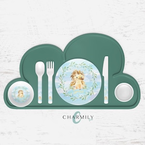 以下が含まれることがあります： 白いプレート、ボウル、スプーン、フォーク、ナイフがついた、緑色の雲の形をしたシリコン製のプレースマット。プレートとボウルには、青い背景と緑の葉の中にハリネズミが描かれた水彩画が施されています。プレースマットには「CHARMILY」の文字が印刷されています。