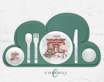 Puede incluir: Un mantel individual de silicona verde en forma de nube con un plato, un tazón y cubiertos blancos. El plato tiene un diseño navideño con una tienda de juguetes y el nombre "HARRY" en él.