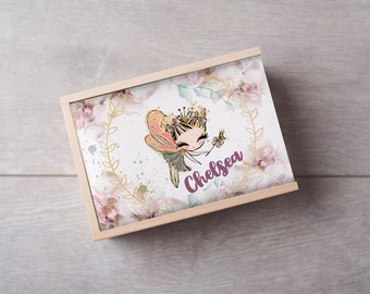 Può includere: Una scatola di legno con un design floreale e una fata dei cartoni animati con una corona e ali. La scatola ha il nome "Chelsea" scritto su di essa.